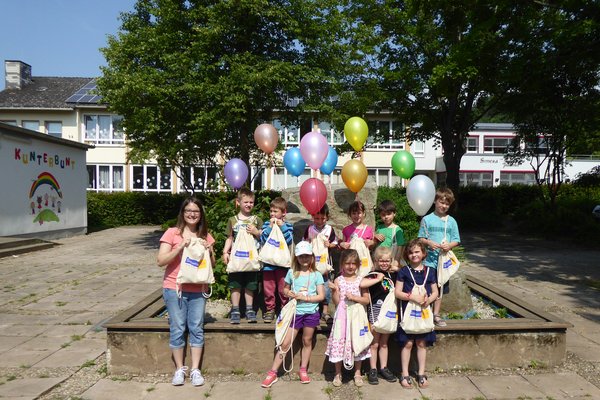 Auf dem Foto sieht man die Kinder vom Kidnergarten Simmertal sowie unsere Marketing-Mitarbeiterin Frau Schneider. Alle halten Turnbeutel mit dem Stadtwerke Kirn GmbH Logo hoch. Außerdme halten die Kinder noch Luftballons in der Hand.